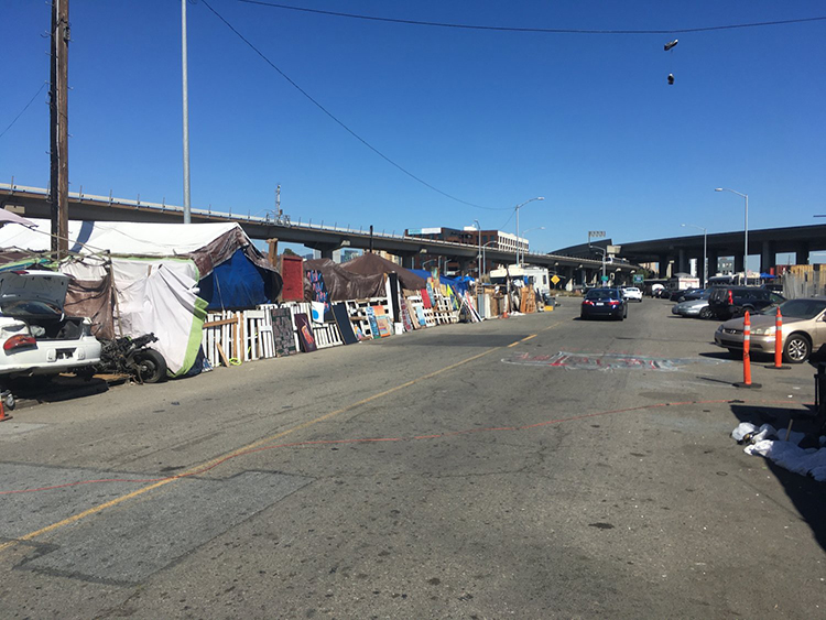 Figure 1. The Fifth Street Natives Encampment (left) framed by Fifth Street, a raised BART (Bay Area Rapid Transit) line, the Interstate 880, and an upscale apartment complex in the distance, Oakland, California, 2021. Photograph by Ben Jameson-Ellsmore.